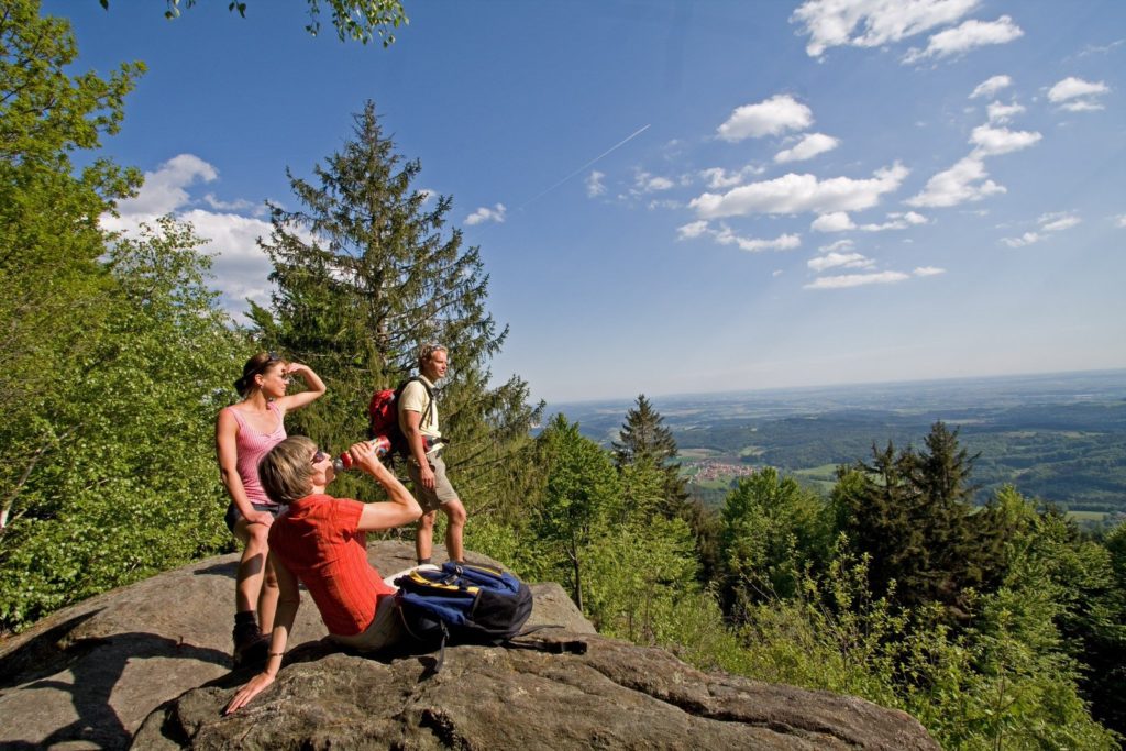Eine Gruppe Menschen sitz auf einem Felsen und schauen ins Tal